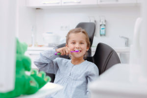 Ein Mädchen mit Zahnbürste putzt in der Zahnarztpraxis die Zähne