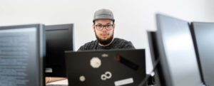 Junger Mann mit Basecap hinter PC Monitor Fotografen für modernes Webdesign in NRW.