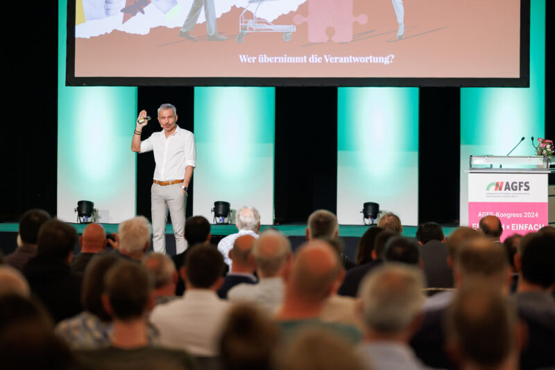 Ein Eventfoto der Dirk Baumbach Fotografie. Das Foto zeigt den Redner auf der Bühne beim Kongress. Im Vordergrund ist das Publikum zu sehen.