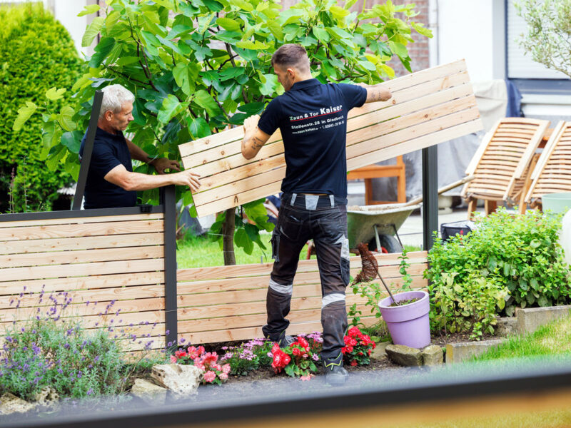 Ein Bauunternehmen für Zäune und Tore. 2 Mitarbeiter bei Ihrer Tätigkeit auf einer Baustelle.